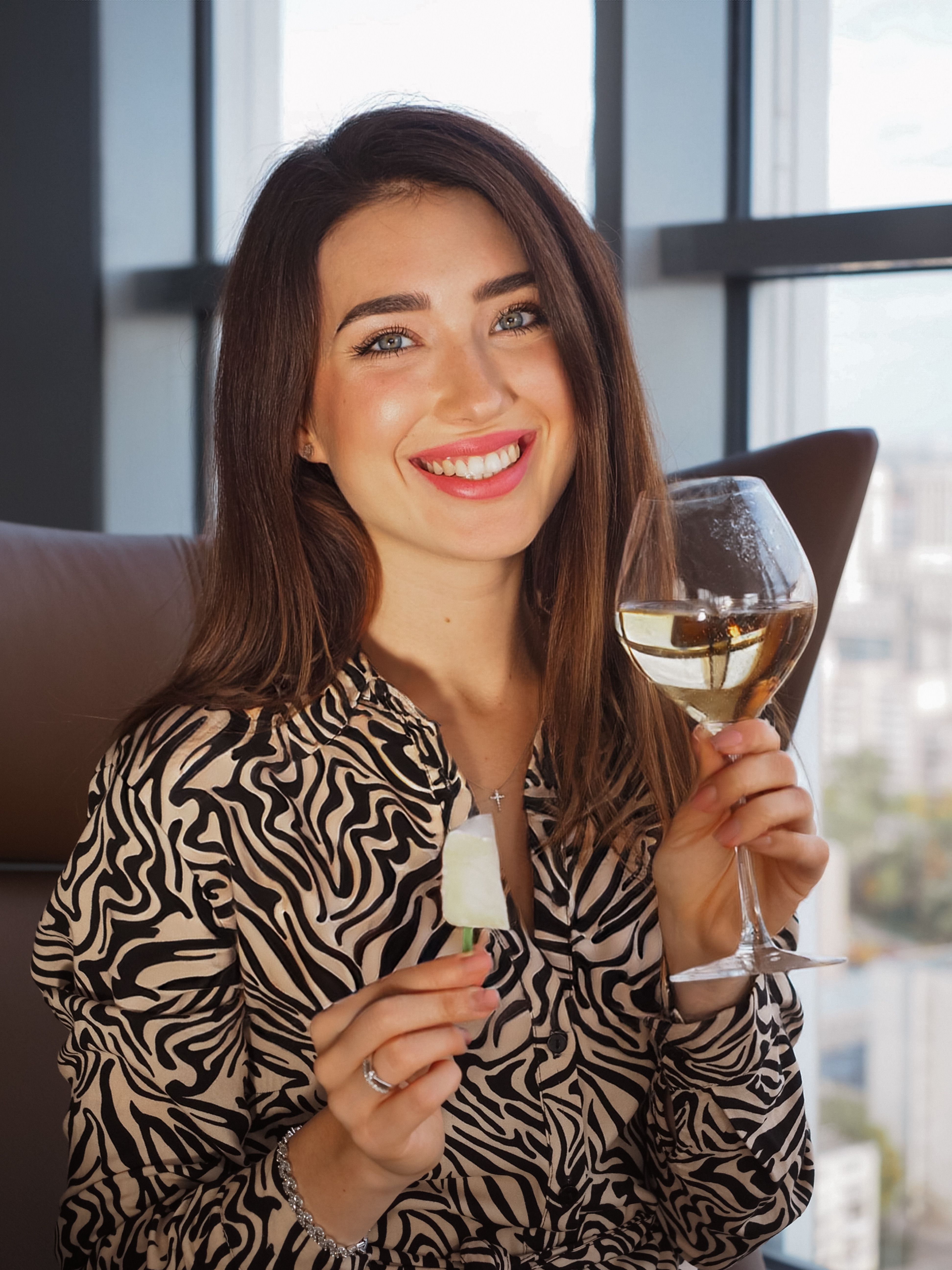 Portrait of a cheerful woman with wine and ice cream indoors, wearing a zebra print.