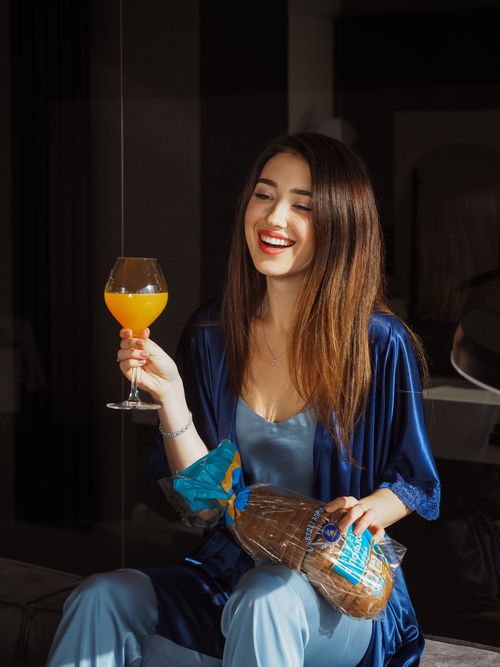 Free Smiling woman in blue attire relaxing with a glass of juice and bread indoors. Stock Photo