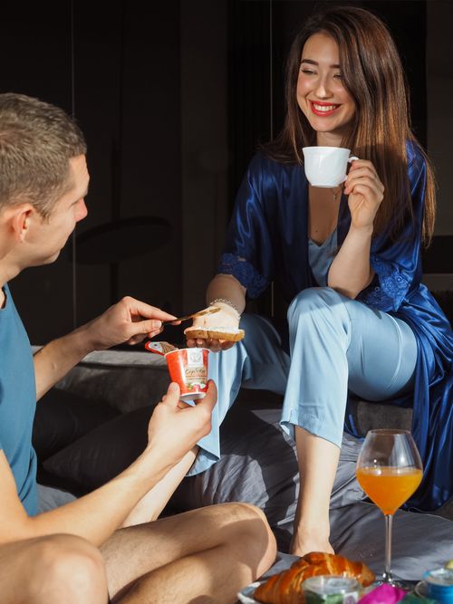 Free Relaxed couple in bed enjoying breakfast with coffee, croissants, and yogurt, highlighting a cozy morning vibe. Stock Photo