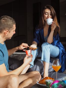 A couple relaxes indoors enjoying breakfast in bed with yogurt and drinks.