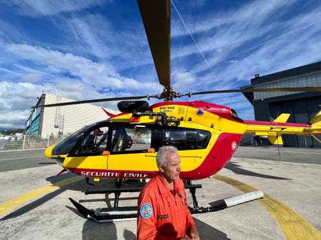 Civil security helicopter on helipad with pilot in uniform during daytime.