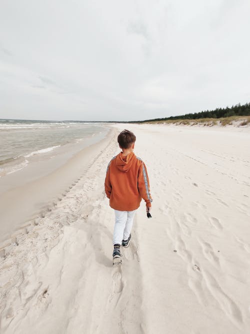 Back View of a Boy in Red Jacket Walking on the Sea Shore