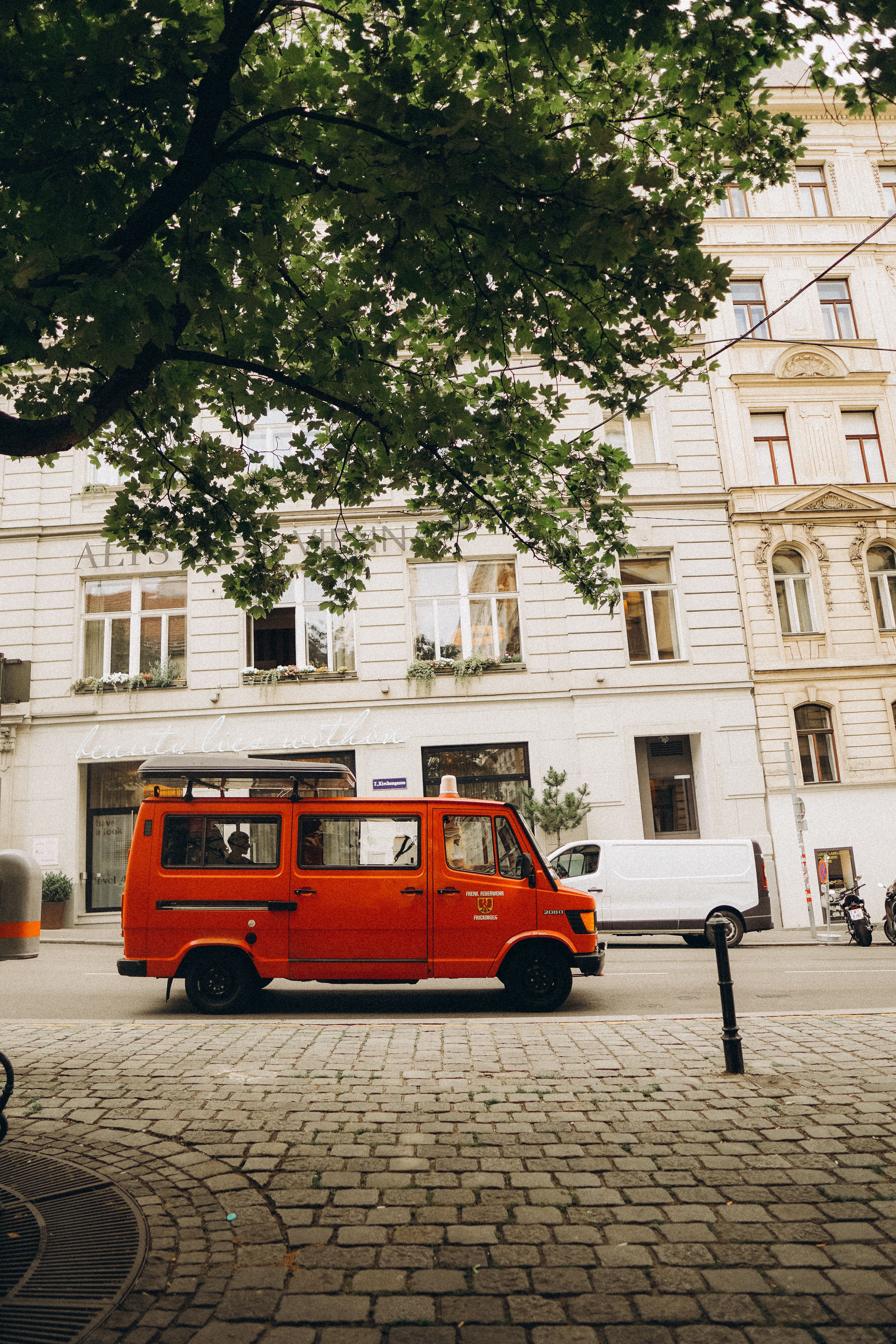A vibrant red van parked on a charming street in Vienna, Austria, under a lush tree.