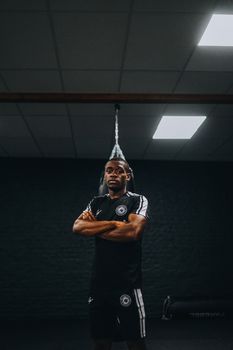 Black male athlete stands confidently in a dimly lit gym, showcasing strength and focus.