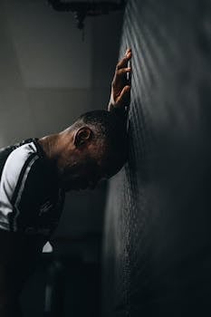 Distraught athlete in sportswear leans head against wall in disappointment.