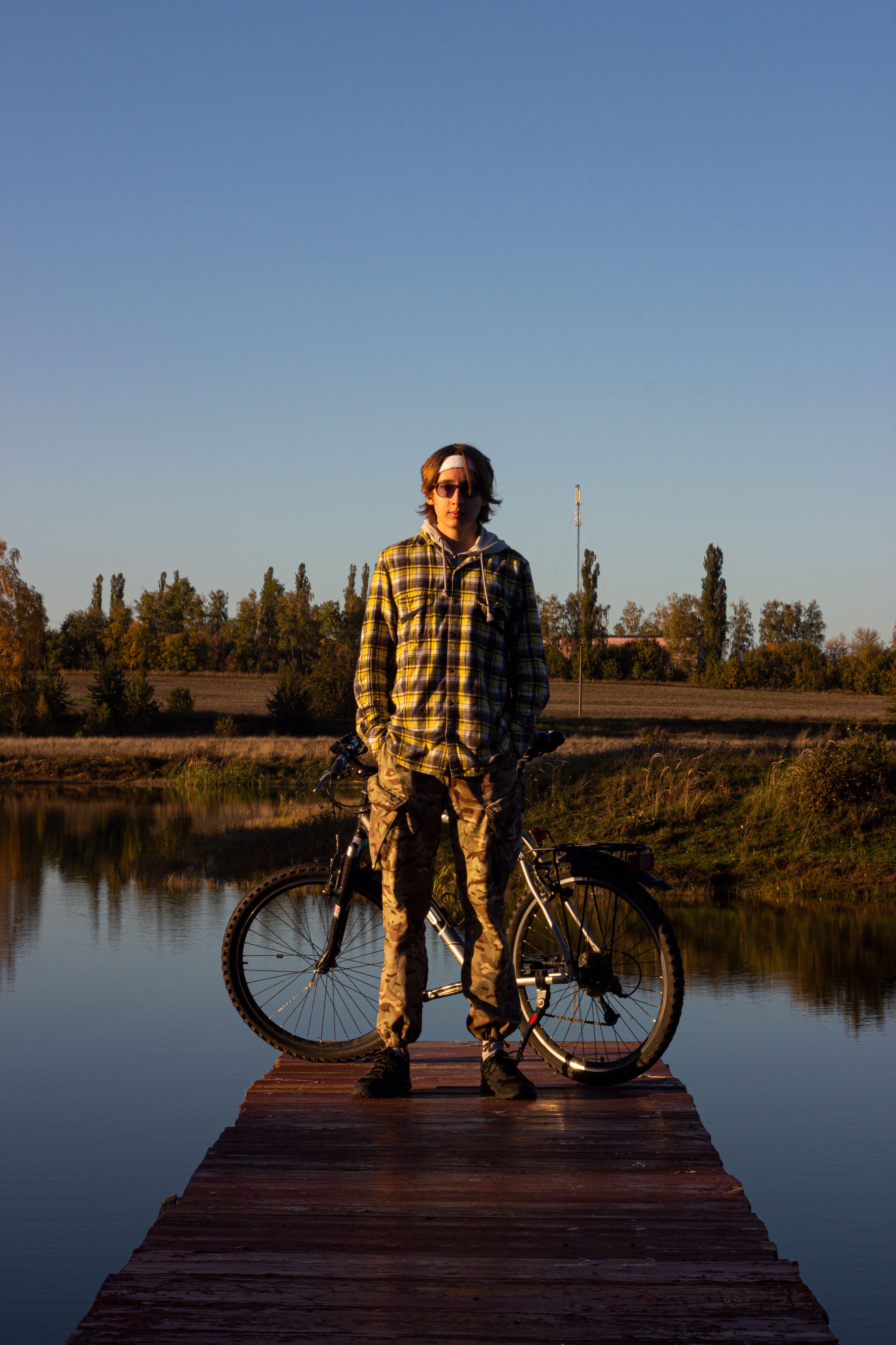 A person stands with a bicycle on a wooden dock by a lake at sunset, showcasing calm outdoor vibes.
