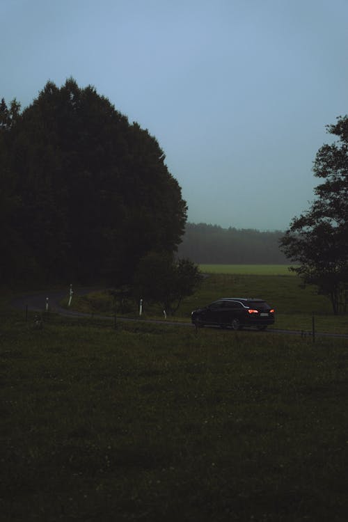 A Black Car Moving on the Road Between Green Grass Field