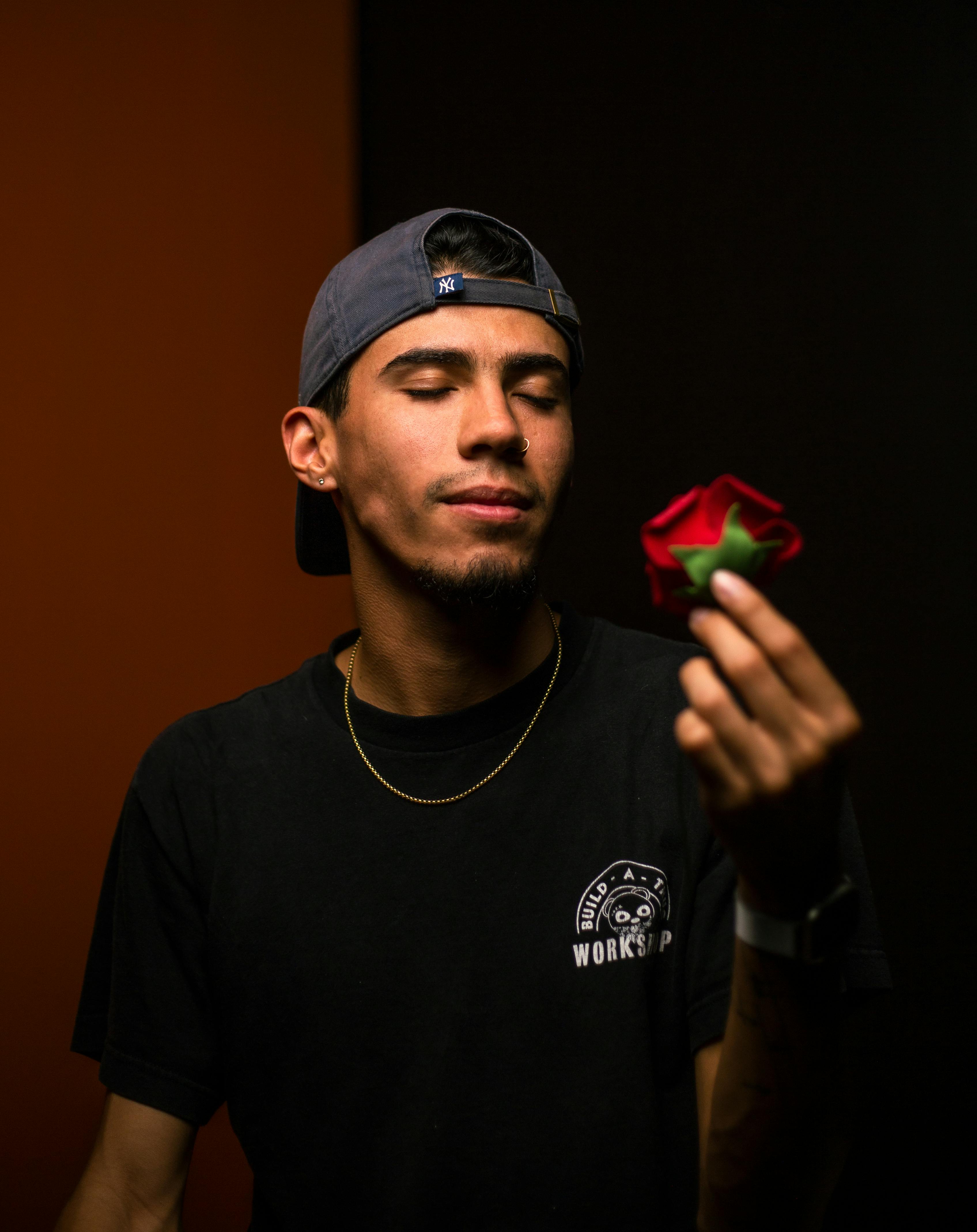 Portrait of a young man with a cap holding a rose and closing his eyes, creating a contemplative mood.