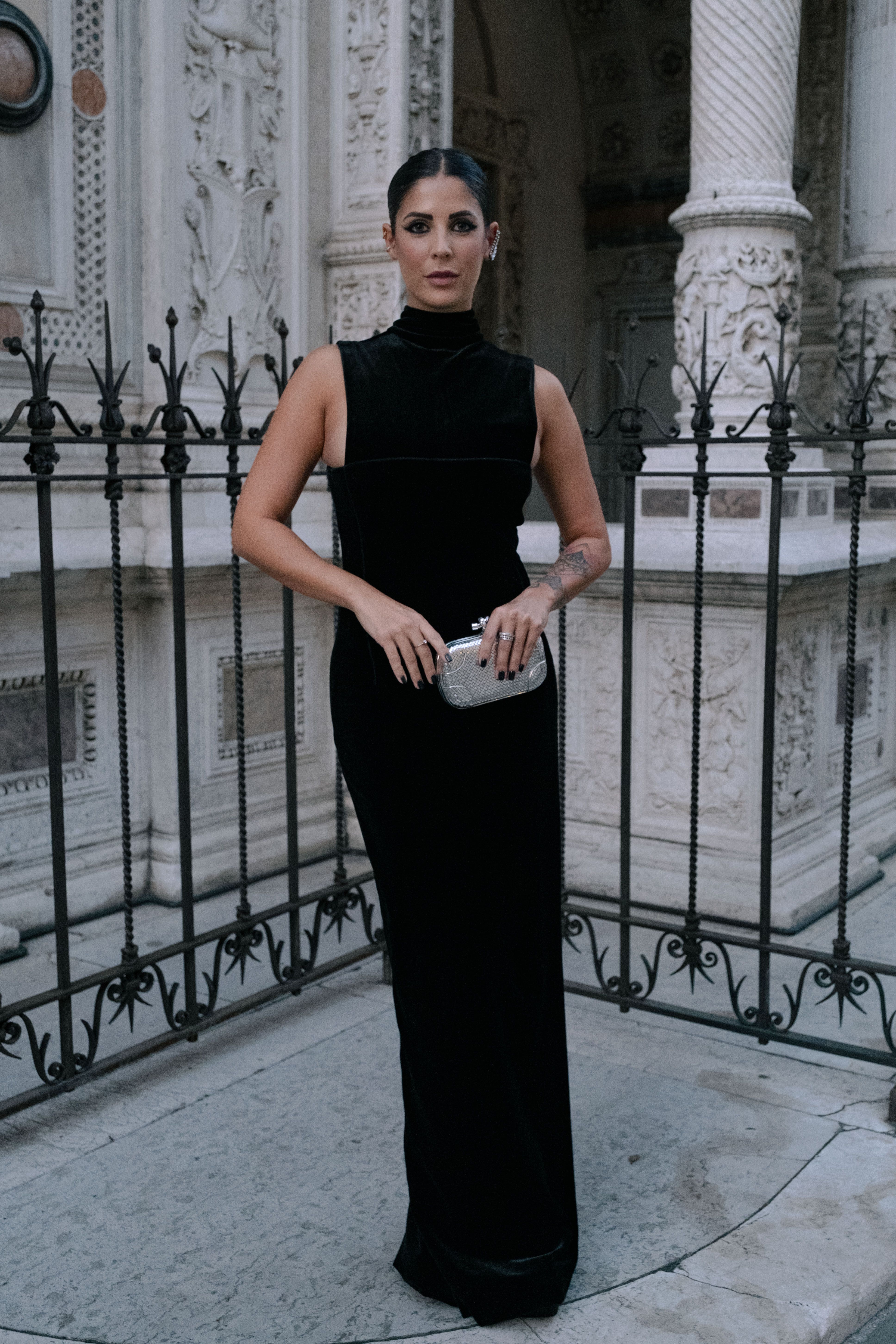 A woman in a black dress poses elegantly at a historical site in Brescia, Italy.