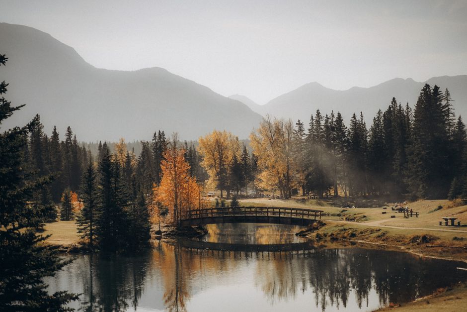 A tranquil autumn scene with a bridge over a lake surrounded by mountains and trees.