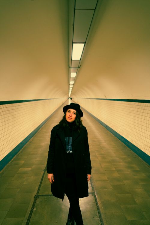 Free A woman in a black coat and hat stands in a tunnel with tiled walls. Stock Photo