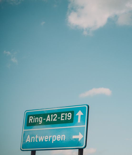 A vertical road sign directing towards Antwerpen under a clear sky.