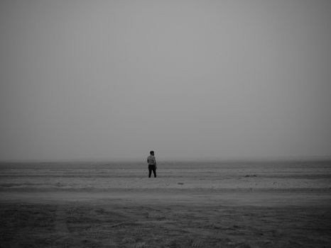 A lone man stands on an empty beach in black and white, conveying solitude and introspection.