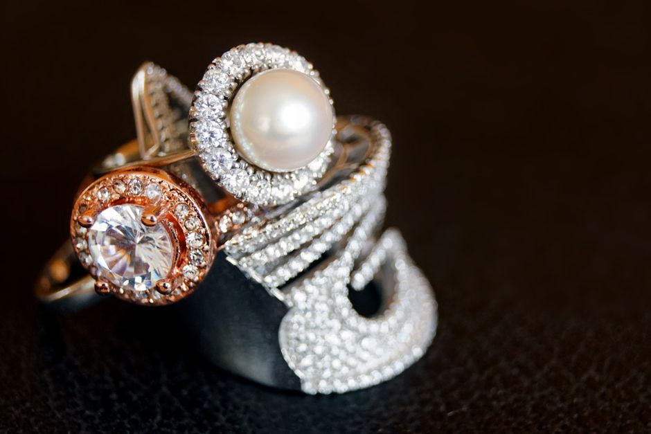 Pearl and gemstone statement rings on a dark reflective surface