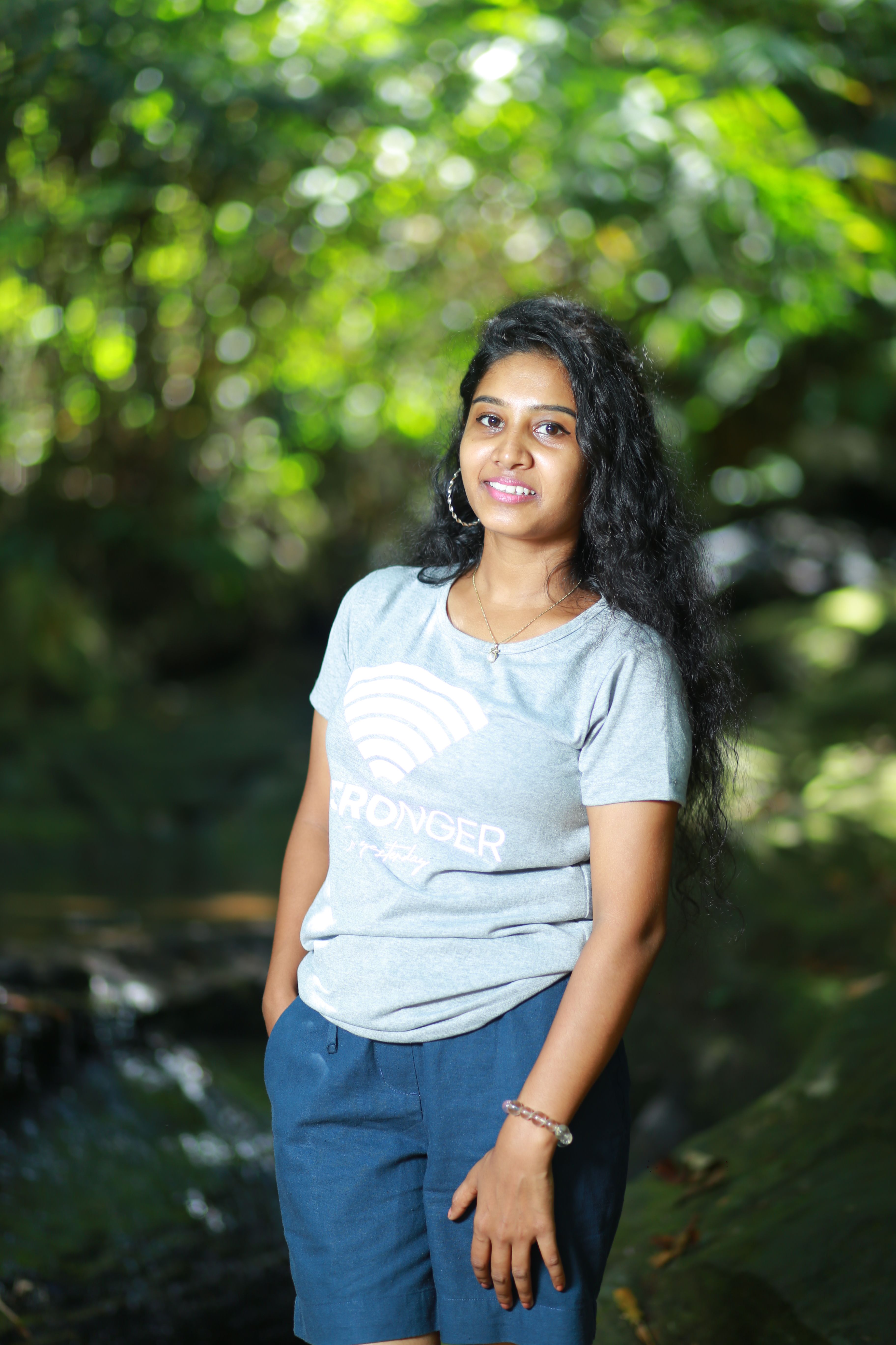 Young Indian woman poses in a scenic forest setting with natural lighting.
