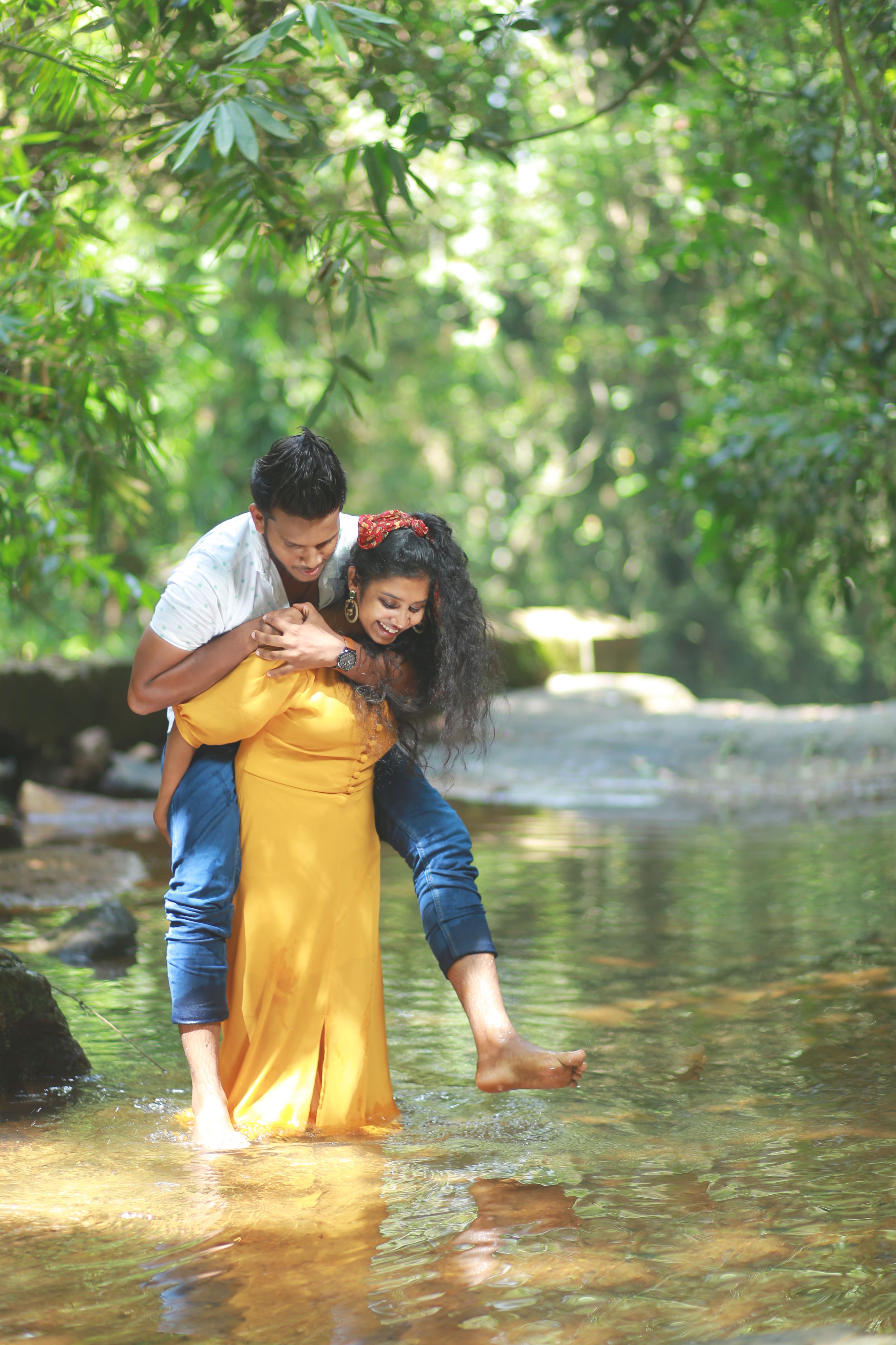 Happy couple standing in a stream, enjoying a playful moment in a lush green forest