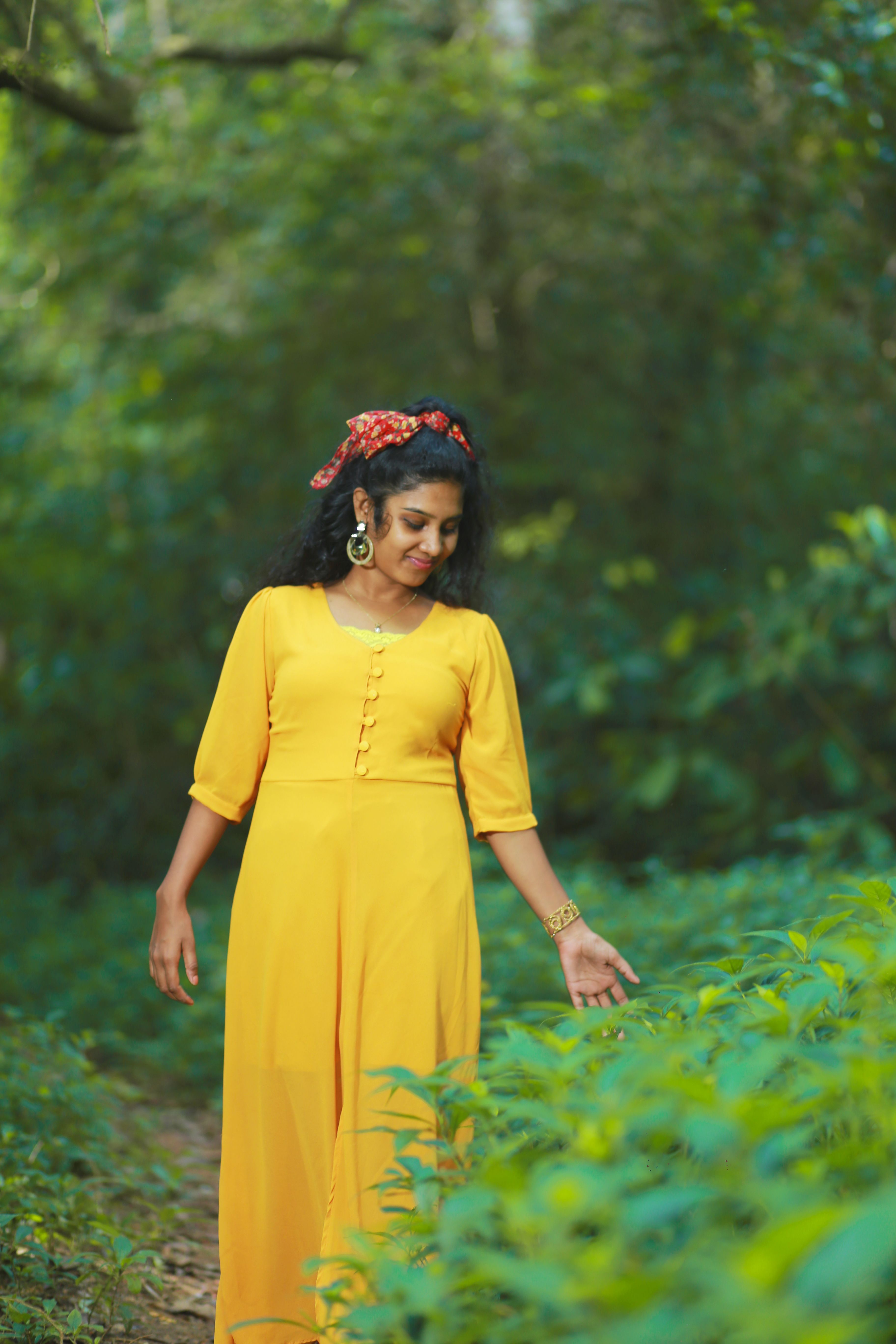 Indian woman in a yellow dress joyfully walking through a lush green forest, conveying harmony and nature.