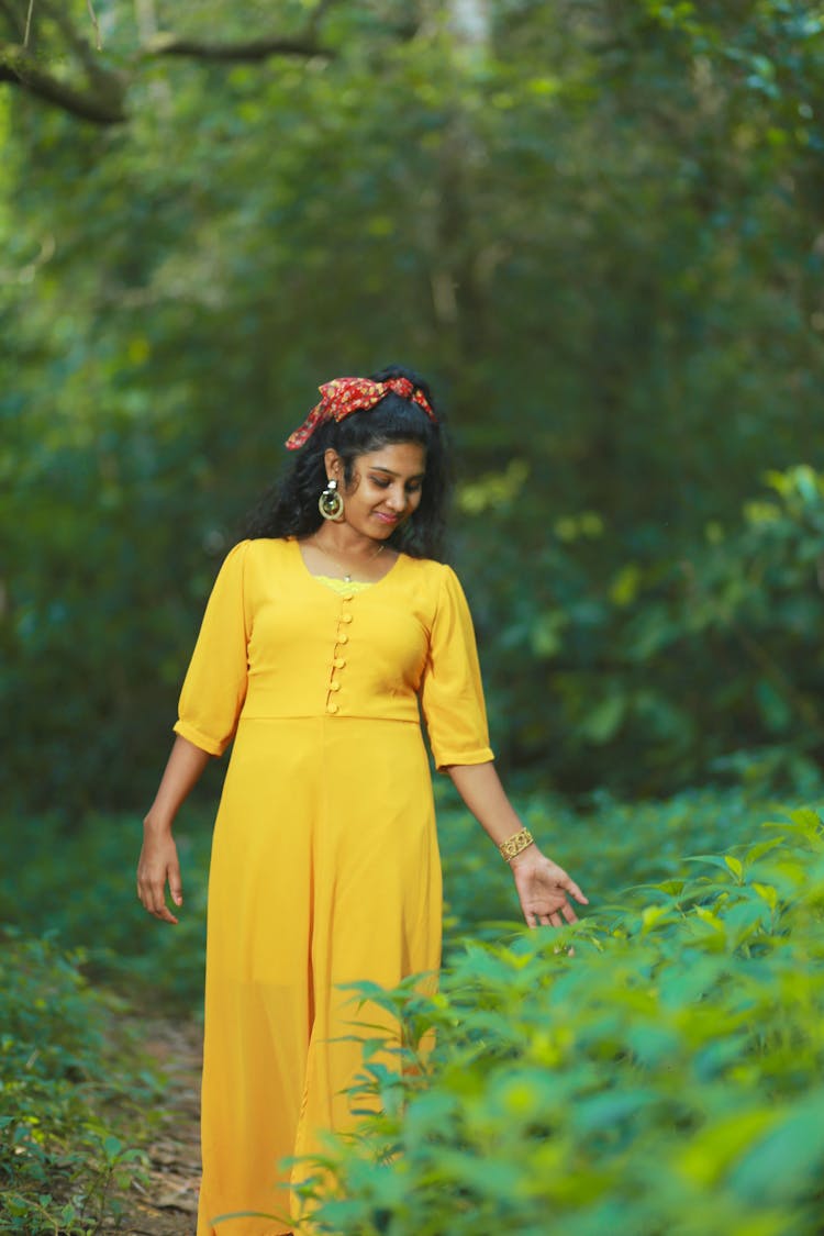 Woman In Yellow Dress Walking Beside The Green Plants 