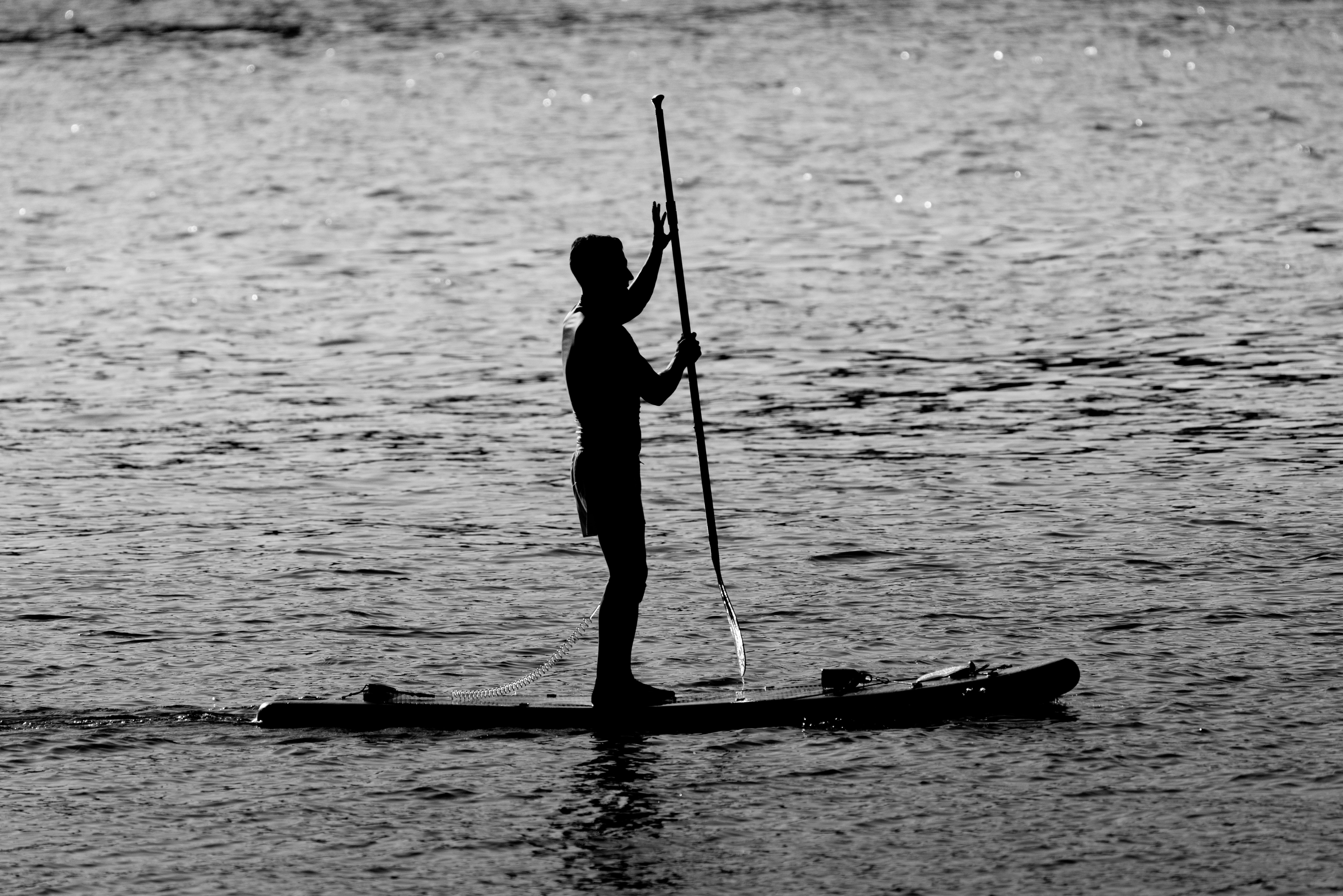 grayscale photo of a man standing on a paddleboard