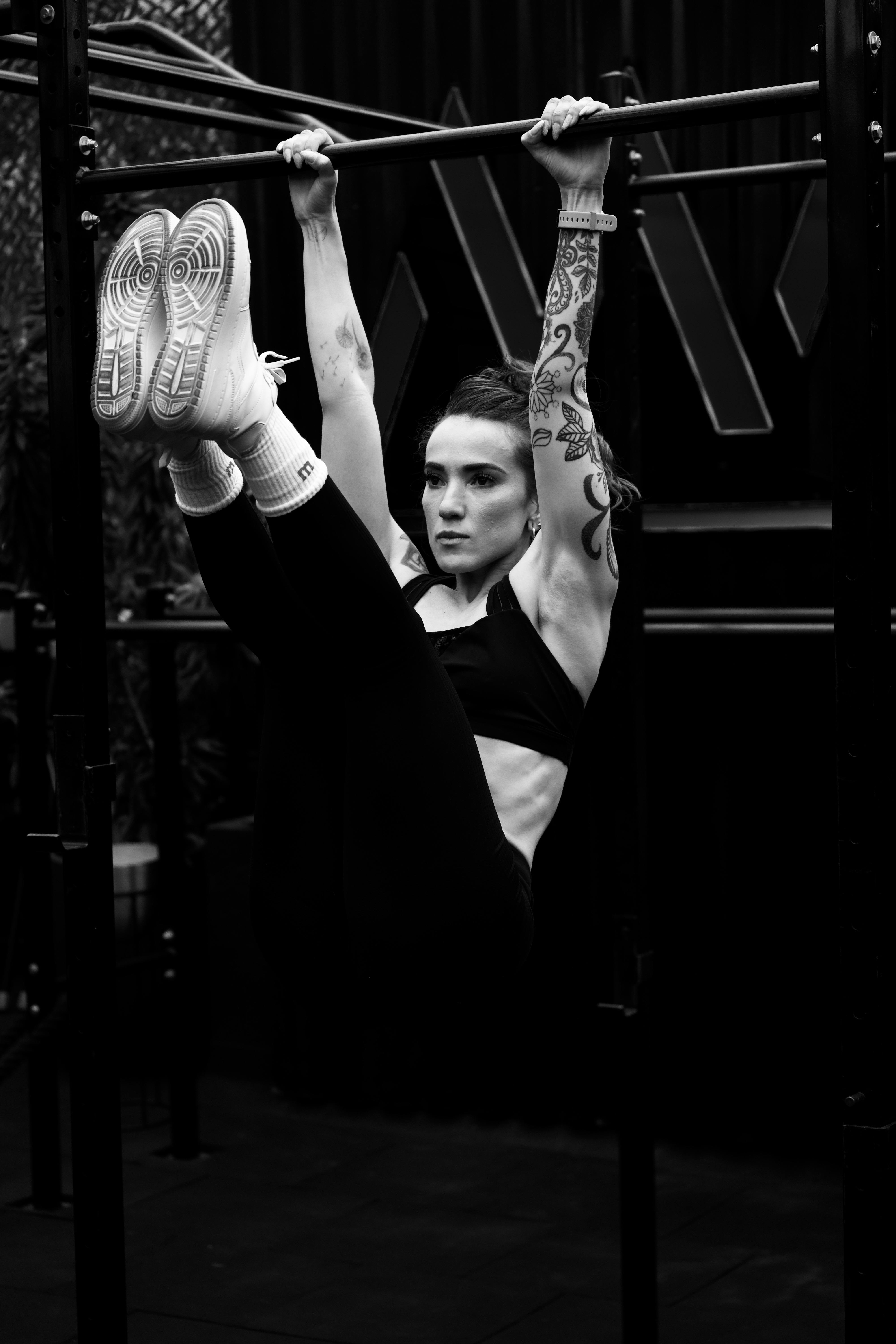Caucasian woman performing pull-ups in a gym showcasing strength and tattoos.
