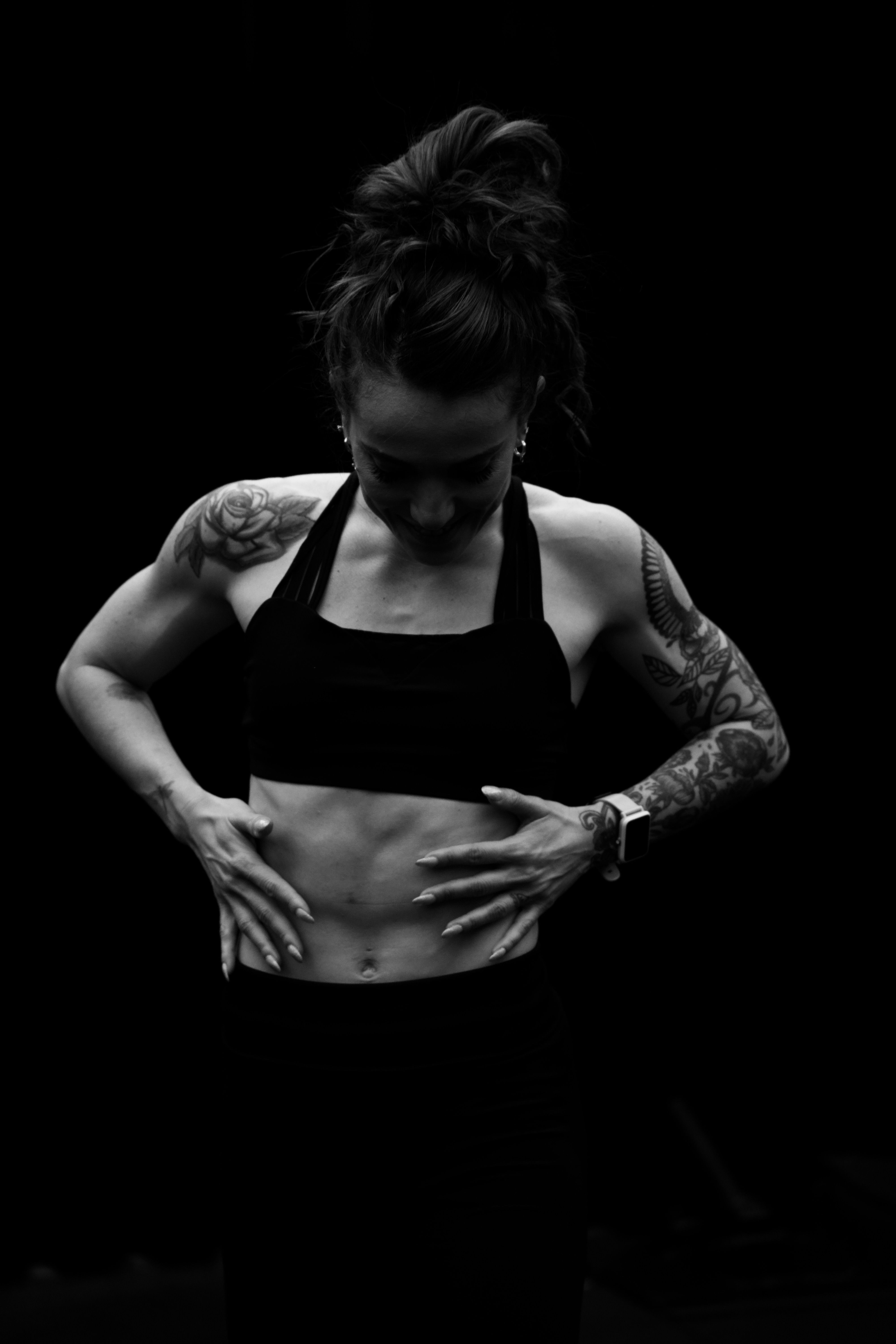 Black-and-white portrait of a tattooed woman in sportswear focusing on fitness.