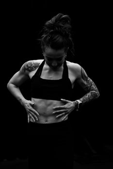 Black-and-white portrait of a tattooed woman in sportswear focusing on fitness.