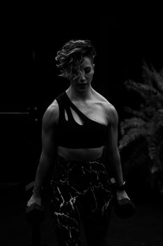 Black and white portrait of a woman in a sports bra lifting weights, showcasing strength and focus.