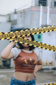 Woman standing behind yellow caution tape in an urban area in Cimahi, Indonesia.