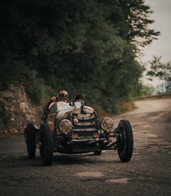 Classic car with two drivers racing on a winding forest road, evoking a timeless adventure.