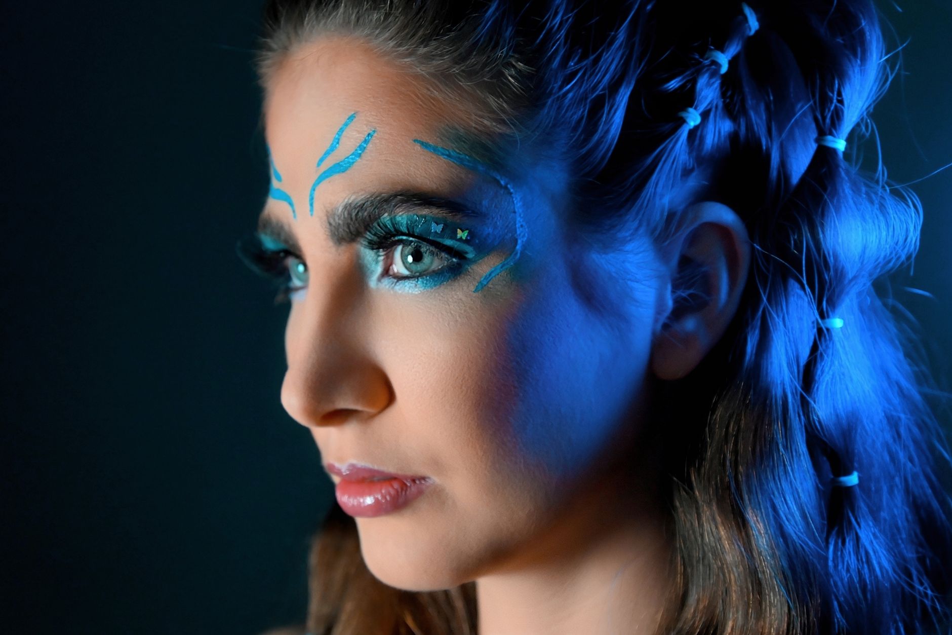 Close-up portrait of a woman with striking blue artistic makeup and braided hair.