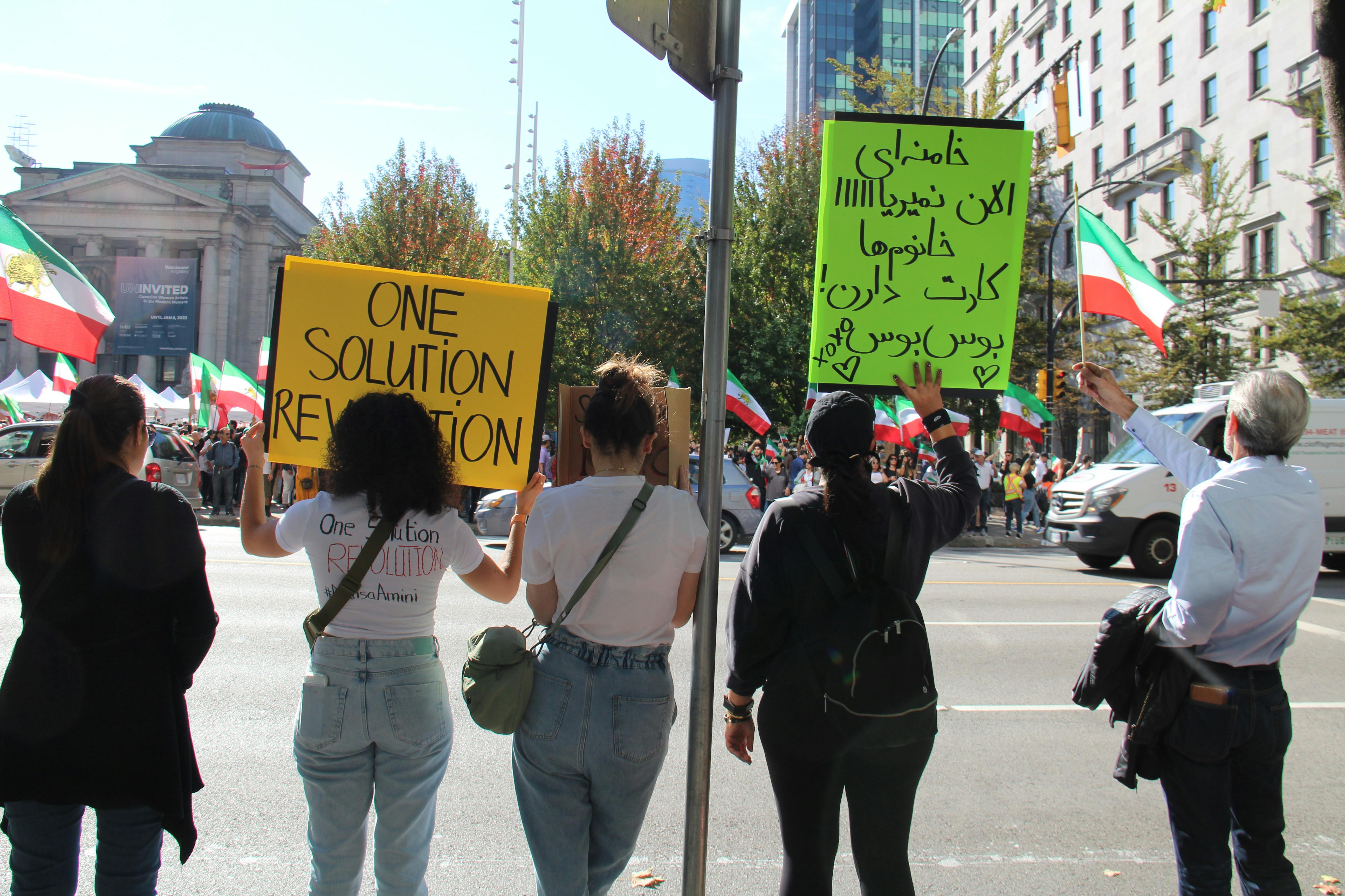 back view shot of people standing on the road side while holding placards