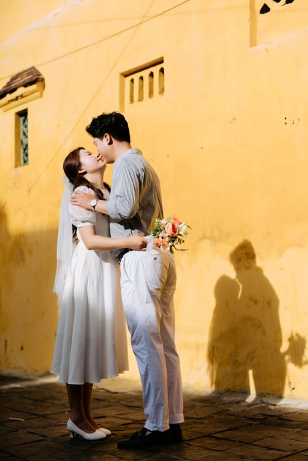 Bride and groom sharing a kiss in front of a vibrant yellow wall, capturing a romantic moment.