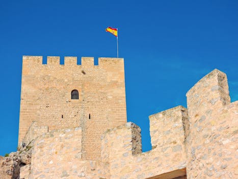 Close-up of Sax Castle in Spain with a vibrant Spanish flag waving under a clear blue sky.