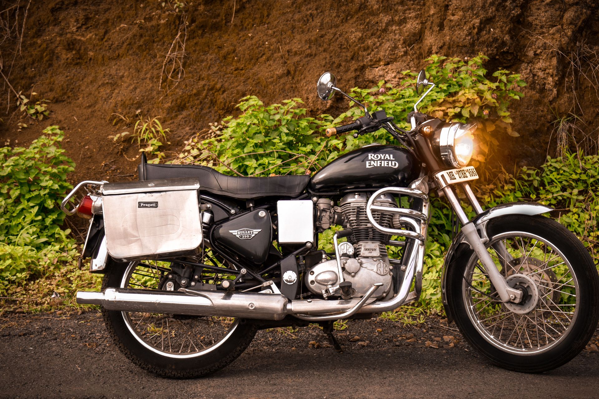Side view of a parked Royal Enfield motorcycle in Amravati, India, with lush greenery backdrop.