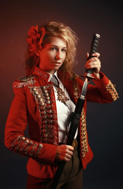 Free Woman in an ornate red blazer holding a sword in a dramatic studio setting. Stock Photo