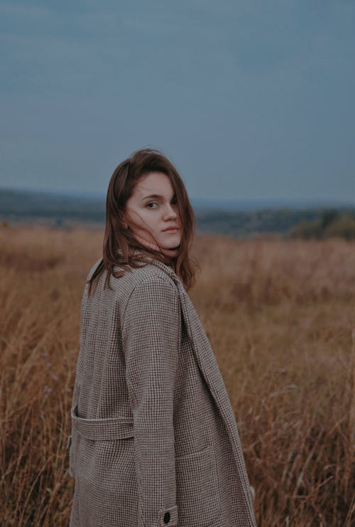 Woman in Brown Coat Standing on Brown Grass Field