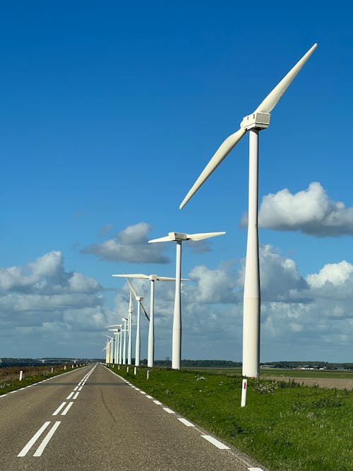 White Wind Turbines Beside an Empty Road Under Blue Sky