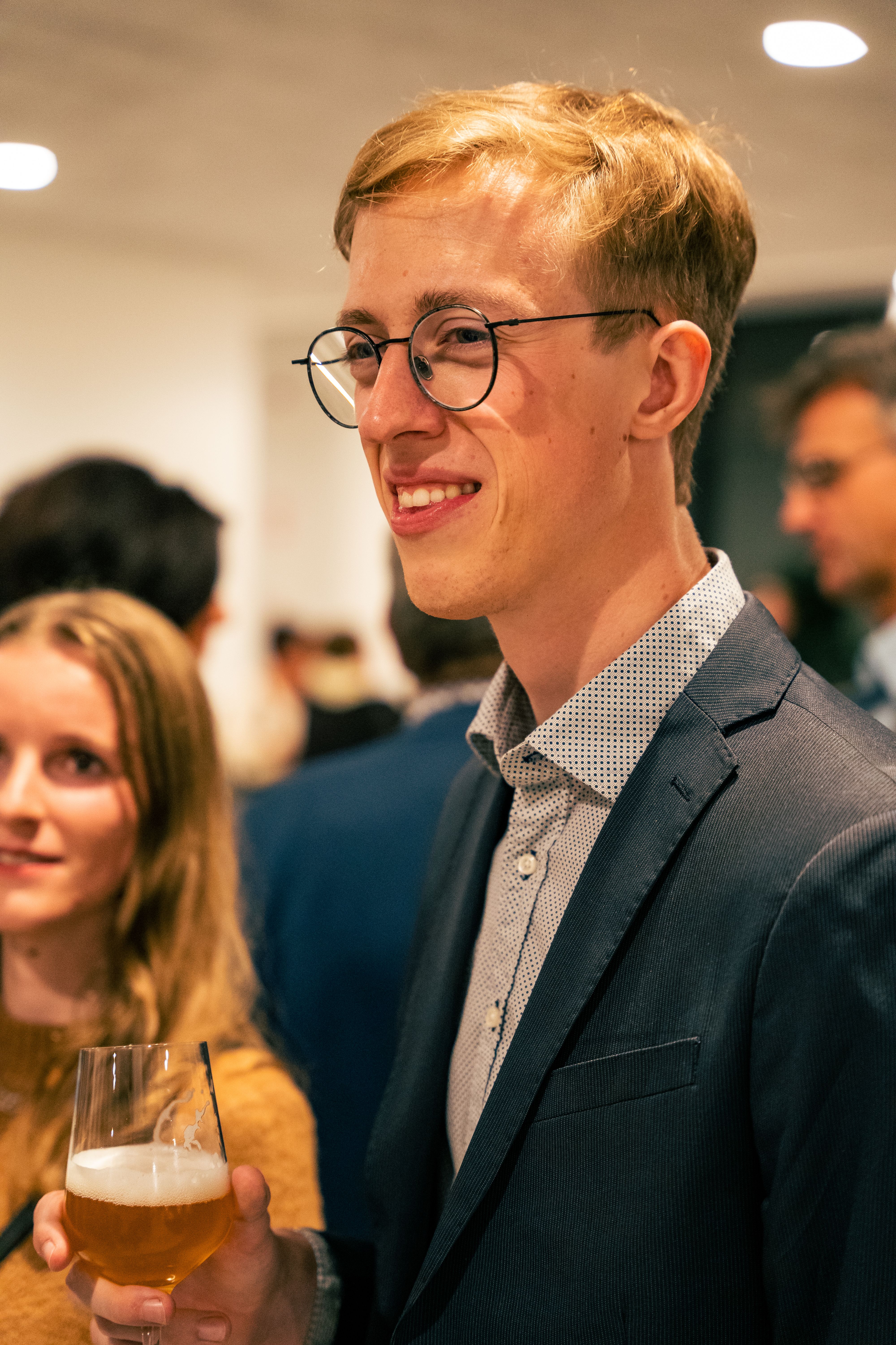 Young man in eyeglasses enjoying a drink at a social event indoors.