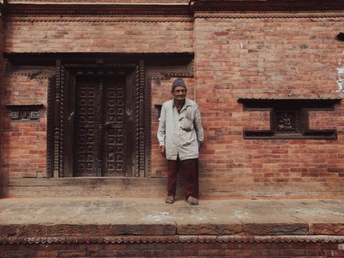 Free A senior man stands by an ornate wooden door and brick wall, capturing cultural heritage. Stock Photo