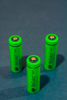 Close-up of three green rechargeable batteries standing on a blue surface.