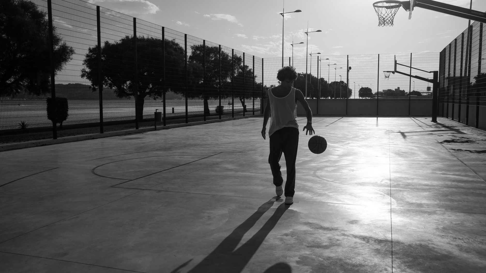 A monochrome shot of a person playing basketball outdoors, emphasizing shadows and movement.
