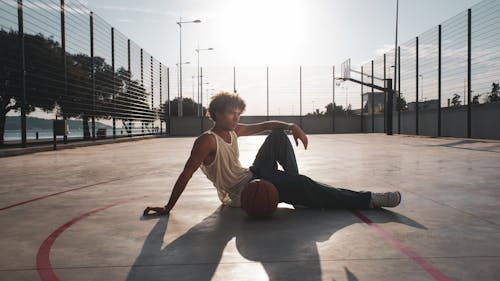 Man in White Tank Top and Black Pants Sitting on Basketball Court