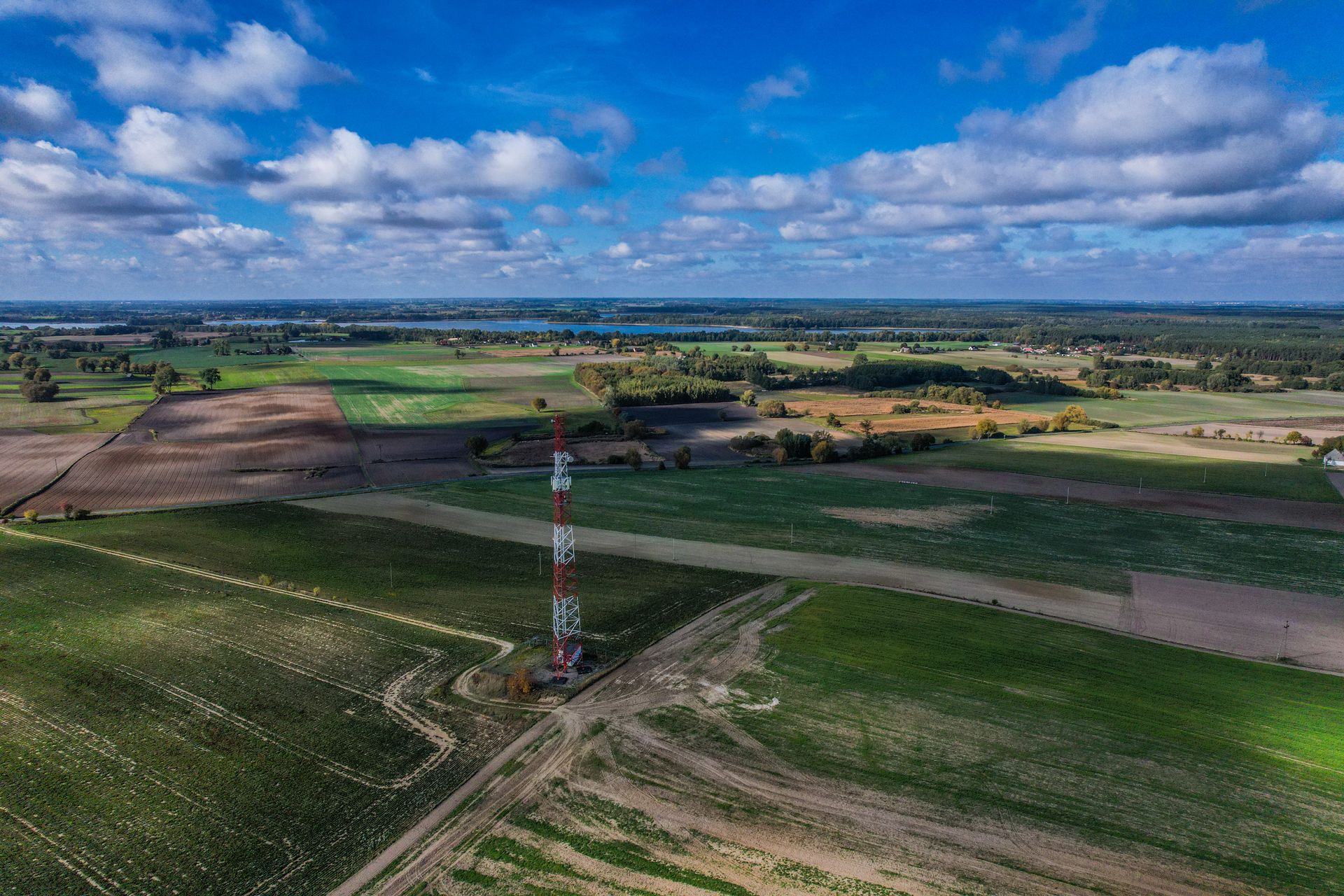 Expansive rural farmland landscape featuring a solitary radio tower under a vibrant blue sky.