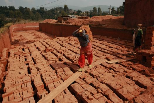 Workers carrying bricks across a kiln in a rural brick-making factory.
