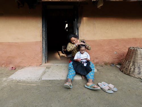A Mother Tying the Hair of Her Daughter while Sitting Near the Open Door