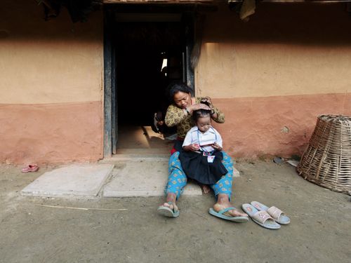 Free A mother braiding her daughter's hair in front of a rural home on a sunny morning. Stock Photo