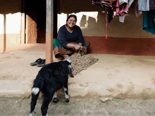 A Happy Woman Sitting Outside a Concrete House Near a Goat