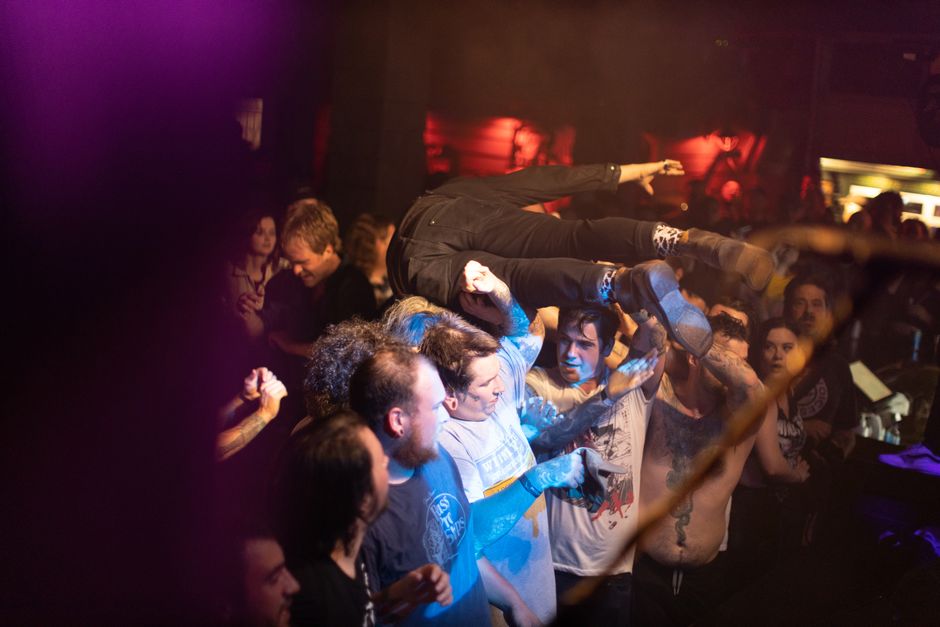 Dynamic scene of crowd surfing and celebration at a live music concert with enthusiastic audience.