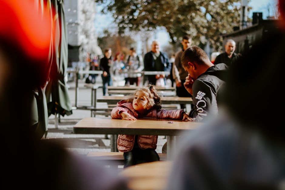 Hombre y niño sentados en una mesa al aire libre con un animado fondo urbano.