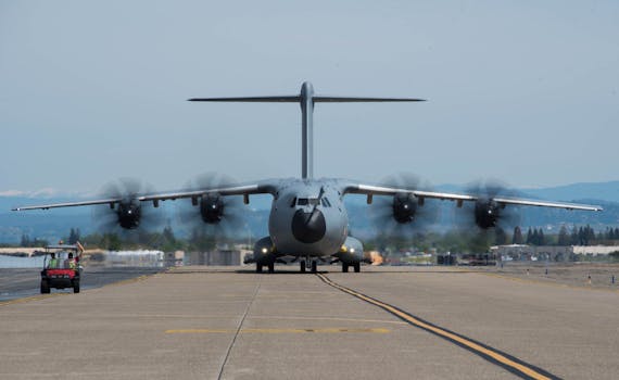 Front view of a military Airbus A400M on the tarmac with spinning propellers outdoors.
